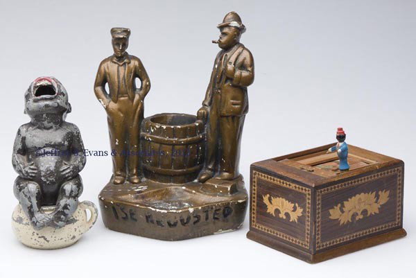 BLACK AMERICANA SMOKING ARTICLES, LOT OF THREE: BLACK AMERICANA SMOKING ARTICLES, LOT OF THREE comprising a two-piece pot-metal baby on potty ash tray/smoker, a plaster Amos and Andy smoking stand, and a wooden cigarette dispenser. First half 20th