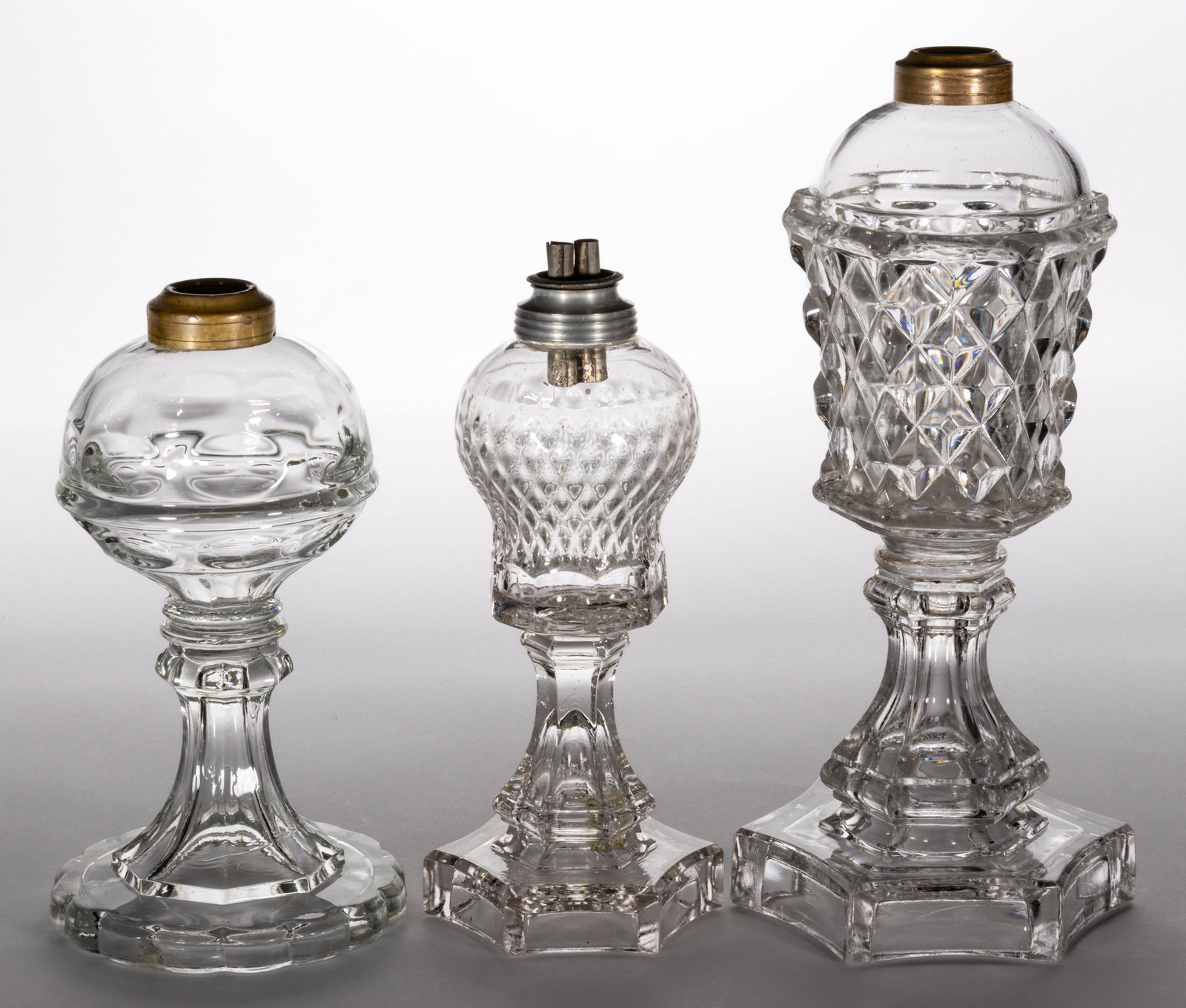 ASSORTED GLASS KEROSENE STAND LAMPS, LOT OF THREE,: ASSORTED GLASS KEROSENE STAND LAMPS, LOT OF THREE,colorless,including a Ring and Punty, a Patrick Slane Diamond, and a Flattened Sawtooth, each having a period collar. Patrick Slane example fitted wit
