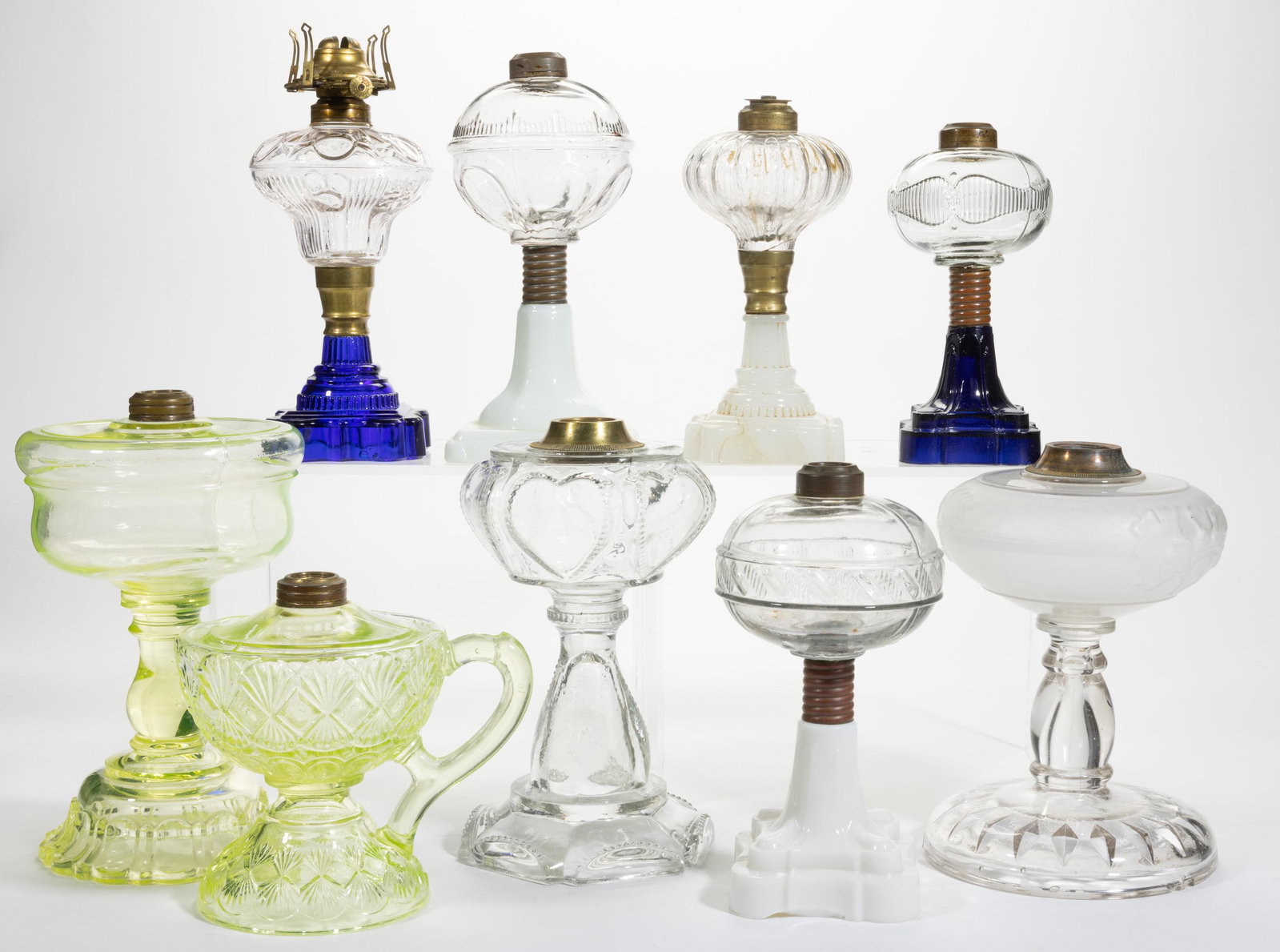 ASSORTED GLASS KEROSENE LAMPS, LOT OF NINE,: ASSORTED GLASS KEROSENE LAMPS, LOT OF NINE,various colors,including an Apollo, a Riverside Heart, and an Atterbury Ribbed Belt, each having a brass collar with one being adapted for electrification.Va