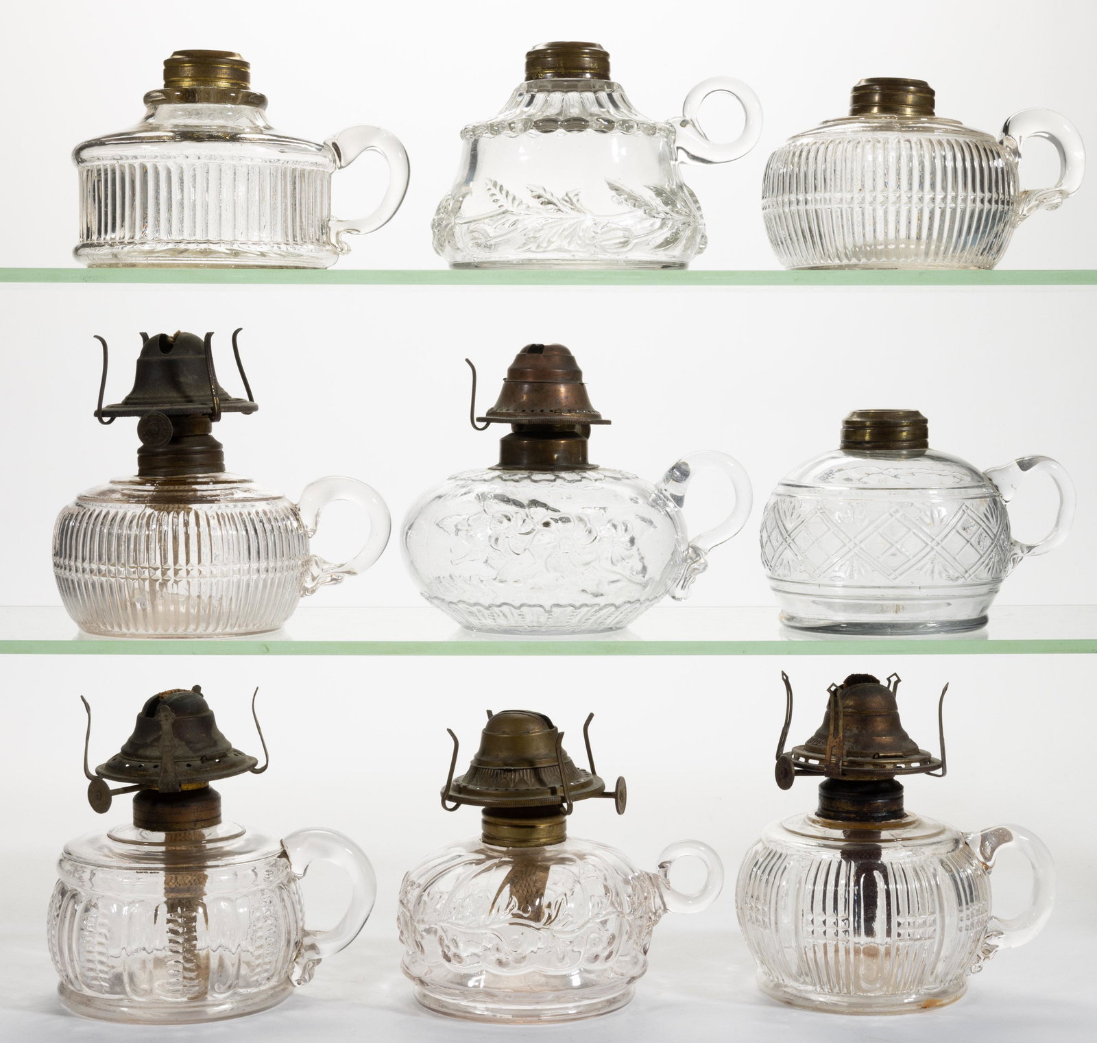 ASSORTED PATTERN KEROSENE FINGER LAMPS, LOT OF NINE: ASSORTED PATTERN KEROSENE FINGER LAMPS, LOT OF NINE,colorless,each with an applied handle, including two Banded Prism examples, a Nosegay, a Poppy Band, Swirled Segments and Vine, and a Zipper and Rib