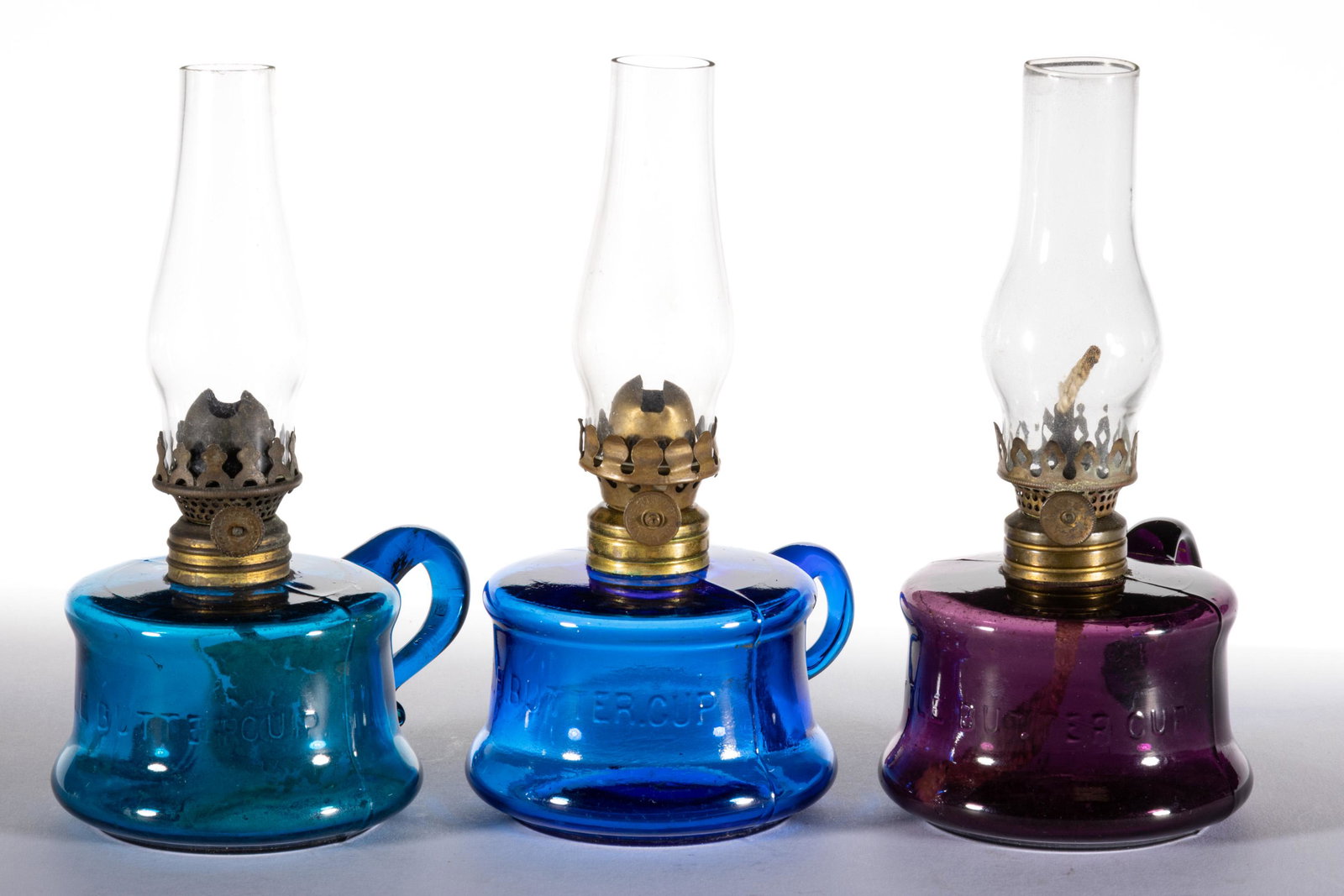 ASSORTED LITTLE BUTTERCUP MINIATURE FINGER LAMPS, LOT OF THREE: ASSORTED LITTLE BUTTERCUP MINIATURE FINGER LAMPS, LOT OF THREE,deep amethyst, peacock blue and sapphire blue,each with an applied handle, concave fonts embossed "LITTLE BUTTERCUP", period collars. Eac