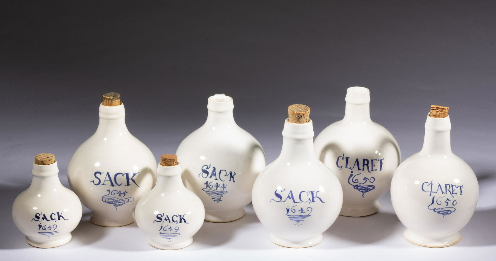 MICHELLE ERICKSON (VIRGINIA, B. 1960) / COLONIAL WILLIAMSBURG REPRODUCTION DELFT EARTHENWARE WINE: MICHELLE ERICKSON (VIRGINIA, B. 1960) / COLONIAL WILLIAMSBURG REPRODUCTION DELFT EARTHENWARE WINE JUGS / BOTTLES, LOT OF SEVEN, tin-glazed, each having blue hand-brushed content description to front,