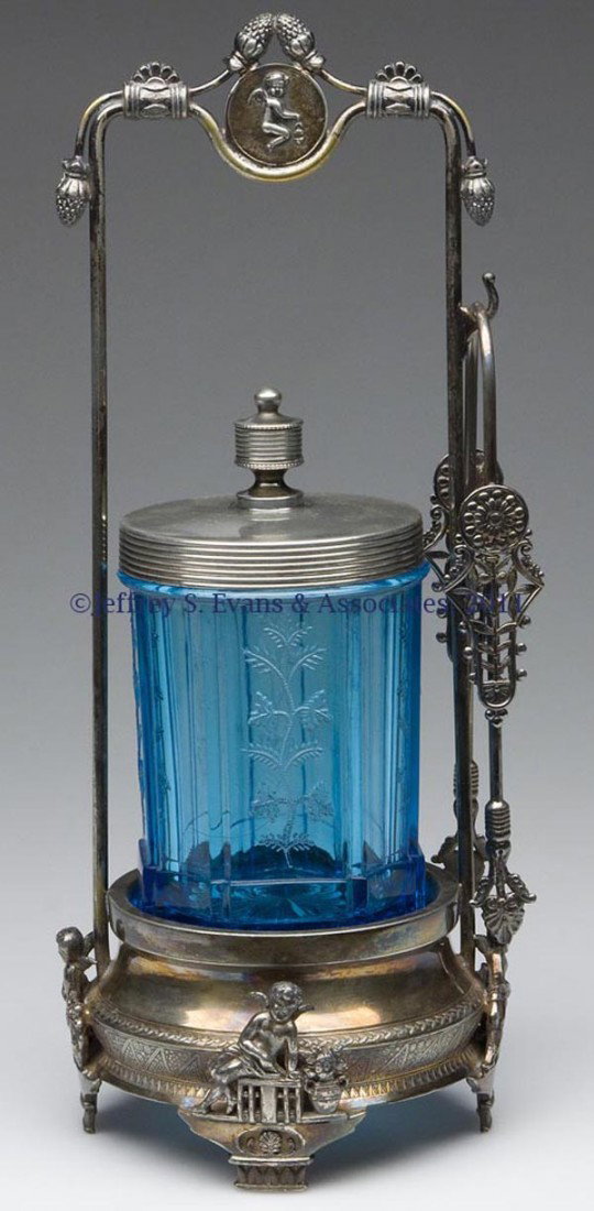 SPRIG PRESSED GLASS PICKLE CASTER: SPRIG PRESSED GLASS PICKLE CASTER, blue, fitted in a Middletown Plate Co. quadruple-plate frame with figural cherubs, with cover and tongs. Fourth quarter 19th century. 11 3/4" HOA, 4 1/4" H, 3 1/8" D