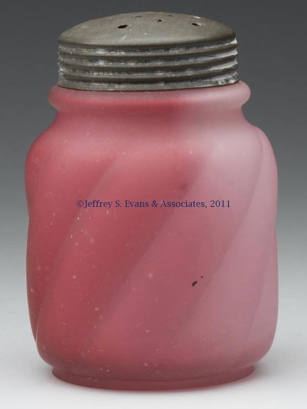 PARIAN SWIRL SUGAR SHAKER: PARIAN SWIRL SUGAR SHAKER, uneven cranberry, satin finish to interior and exterior, period lid. Northwood Glass Co. Fourth quarter 19th century. 4 1/2" h overall. Provenance: Estate collection of Doro