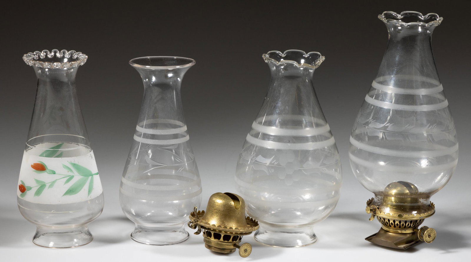 ASSORTED KEROSENE LIGHTING NO. 1 LATE-LIP BURNERS AND CHIMNEYS, LOT OF FOUR: ASSORTED KEROSENE LIGHTING NO. 1 LATE-LIP BURNERS AND CHIMNEYS, LOT OF FOUR, comprising of two setups, each fitted on a period E. Miller & Co lip burner, one burner fitted with a sliding refi
