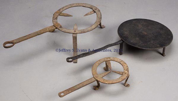 THREE WROUGHT-IRON HEARTH ARTICLES: THREE WROUGHT-IRON HEARTH ARTICLES, comprising two trivets and a revolving griddle, each raised on three feet. Probably 18th and 19th century. 12 1/2" to 21" L. Provenance: Estate collection of Doroth