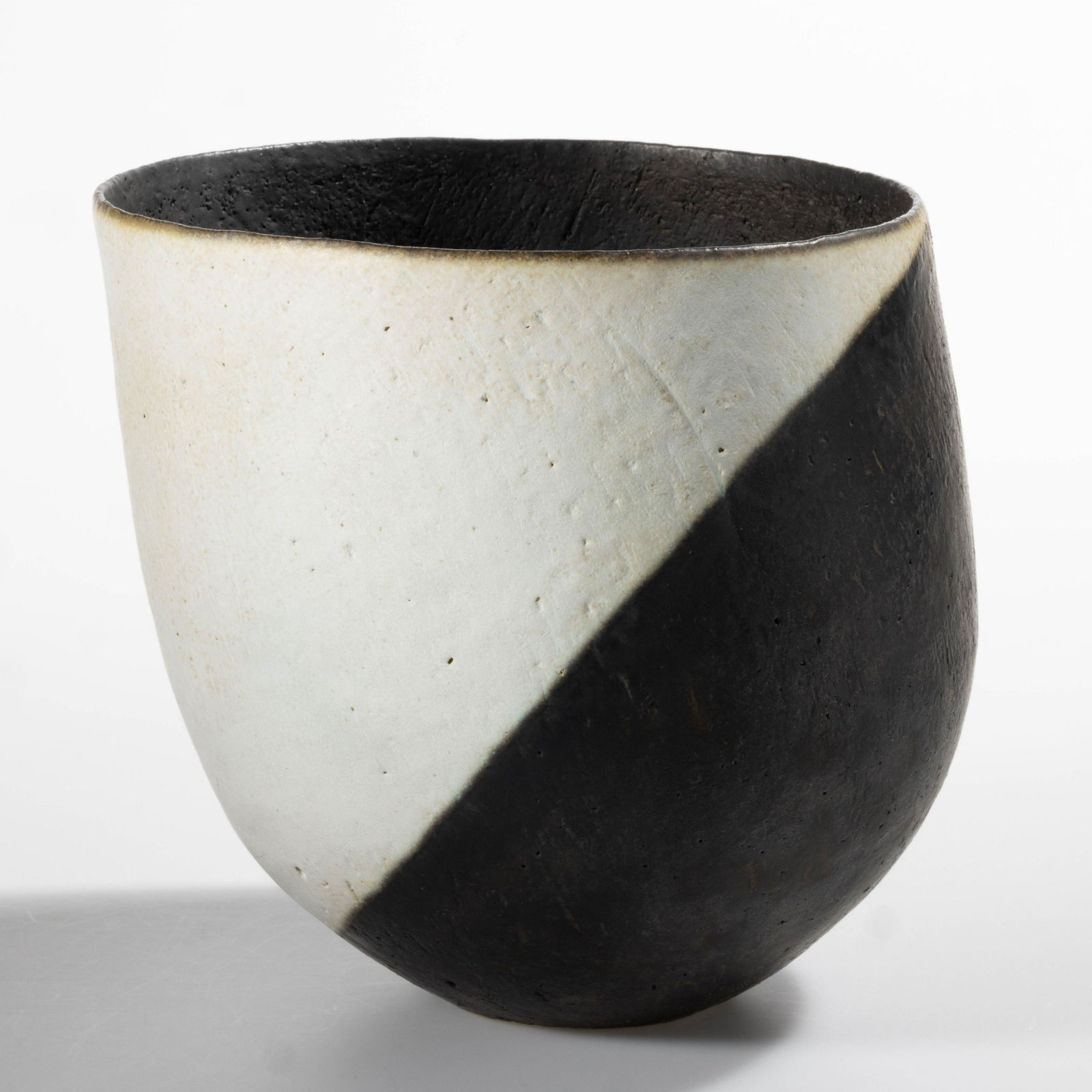 JOHN WARD (ENGLISH, 1938-2023) STUDIO POTTERY STONEWARE BOWL: JOHN WARD (ENGLISH, 1938-2023) STUDIO POTTERY STONEWARE BOWL, slightly leaning deep form with an asymmetric rim, having matte black and white glaze. Impressed "JW" to underside. Fourth