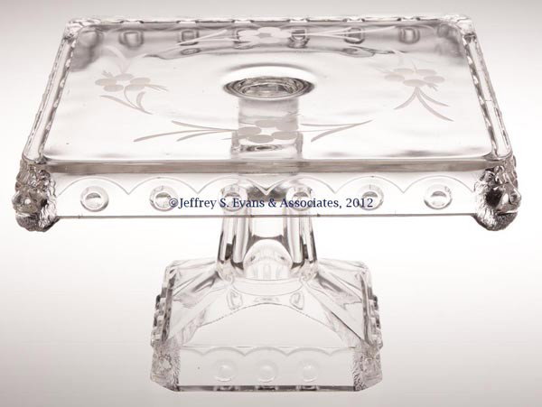 ATLANTA / SQUARE LION CAKE STAND: ATLANTA / SQUARE LION CAKE STAND, colorless, with engraved floral decoration. Fostoria Glass Co. Late 19th/early 20th century. 6" H, 9" SQ. Provenance: Jerry Lynn Wood estate, Dequincy, LA.