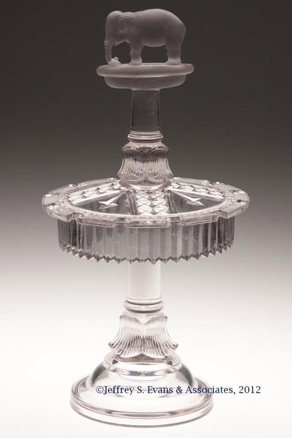 JUMBO SPOON RACK: JUMBO SPOON RACK, colorless with frosted finish to elephant and platform, without embossed patent date. Canton Glass Co. Fourth quarter 19th century. 11 1/8" HOA, 5 3/4" DOA. Provenance: Jerry Lynn Wo