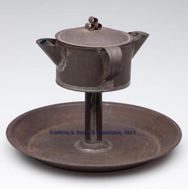 SHEET IRON DOUBLE-SPOUT FAT LAMP ON STAND: SHEET IRON DOUBLE-SPOUT FAT LAMP ON STAND, cylinder-form reservoir with cover fitted with a strap handle and two spouts, each with a copper wick support, supported on a straight stem and large saucer 