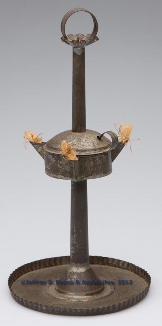 SHEET IRON TRIPLE-SPOUT FAT LAMP ON STAND: SHEET IRON TRIPLE-SPOUT FAT LAMP ON STAND, cylinder-form reservoir with cover which slides one a central shaft for filling, strap ring handle, saucer base with crimped rim. 19th century. 11" HOA, 5 3/