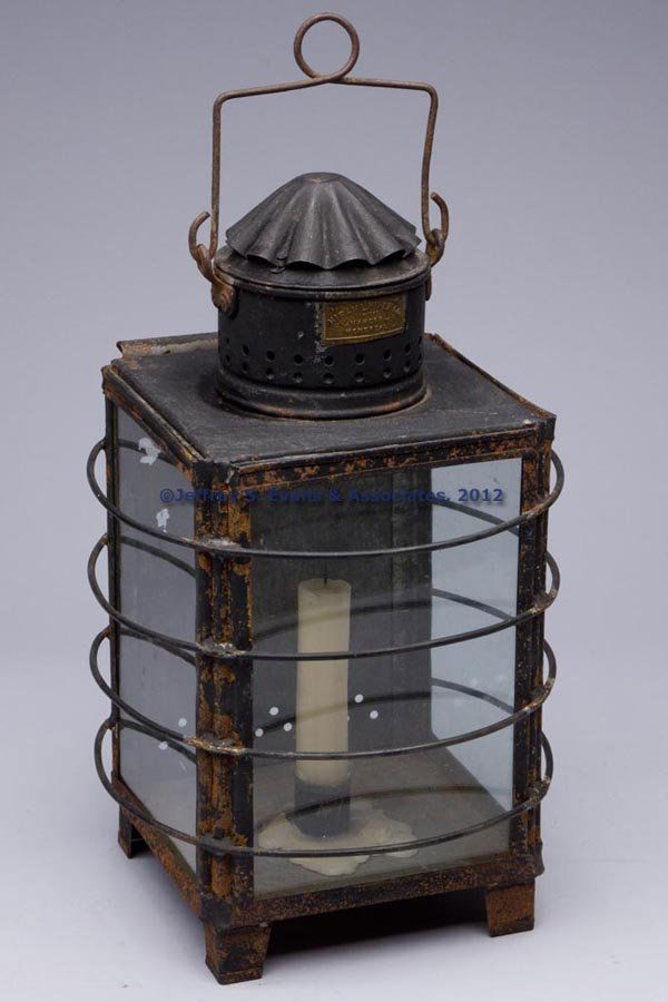 HIRAM L. PIPER CO SHEET IRON CANDLE LANTERN: HIRAM L. PIPER CO SHEET IRON CANDLE LANTERN, square form with bail handle, supported on short legs, three sides with colorless glass panes and contoured guards, reverse with a sliding door, single soc