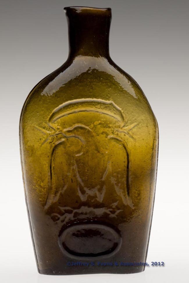 GII-86 EAGLE PICTORIAL FLASK: GII-86 EAGLE PICTORIAL FLASK, olive amber, half-pint, sheared mouth, faint rough pontil mark. New England, possibly Granite Glass Works. 1840-1860. 6" H. "Provenance: The Thomas Dale Barnes estate col