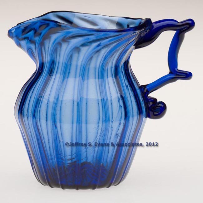 PATTERN-MOLDED CREAMER: PATTERN-MOLDED CREAMER, sapphire blue, barrel-form body with sharp medial shoulder, molded with 16 vertical ribs swirled to the right at the plain rim, elaborate applied solid handle with thumbrest an
