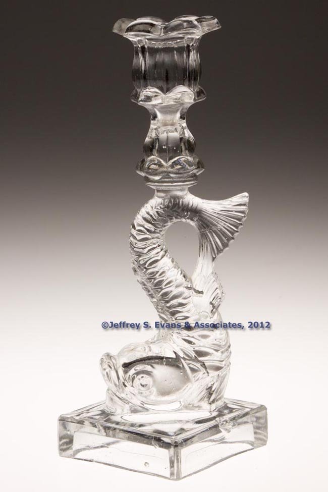 PRESSED DOLPHIN SINGLE-STEP CANDLESTICK: PRESSED DOLPHIN SINGLE-STEP CANDLESTICK, colorless, six-petal socket with lower extension, raised on a large dolphin-form standard and square base, wafer construction. Probably Boston & Sandwich Glass