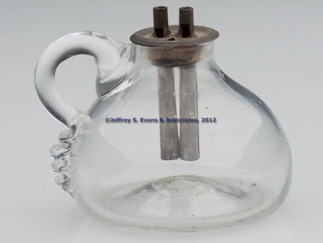 FREE-BLOWN WHALE OIL SPARKING LAMP: FREE-BLOWN WHALE OIL SPARKING LAMP, colorless, applied handle, rough pontil mark. Fitted with a tin and cork double-tube drop-in burner. 1820-1840. 1 7/8" H to top of font, 2" D base. Provenance: From