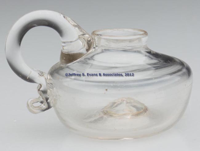 FREE-BLOWN SPARKING LAMP: FREE-BLOWN SPARKING LAMP, colorless, compressed globular font, applied handle, rough pontil mark. 1820-1840. 1 1/2" H to top of font, 1 3/8" D base. Provenance: From the collection of Abigail and the 