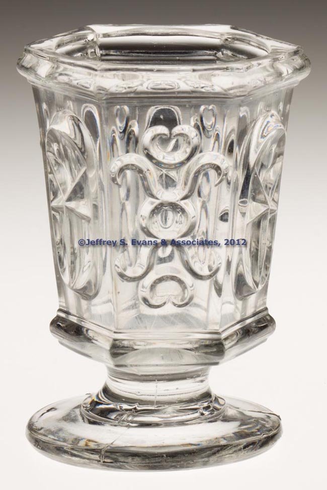 PRESSED STAR AND PUNTY VARIANT SPOON HOLDER / SPIL: PRESSED STAR AND PUNTY VARIANT SPOON HOLDER / SPILL, colorless lead glass, featuring an armorial-type device on alternating panels replacing the usual double circles, rough pontil mark. 1850-1870. 4 5