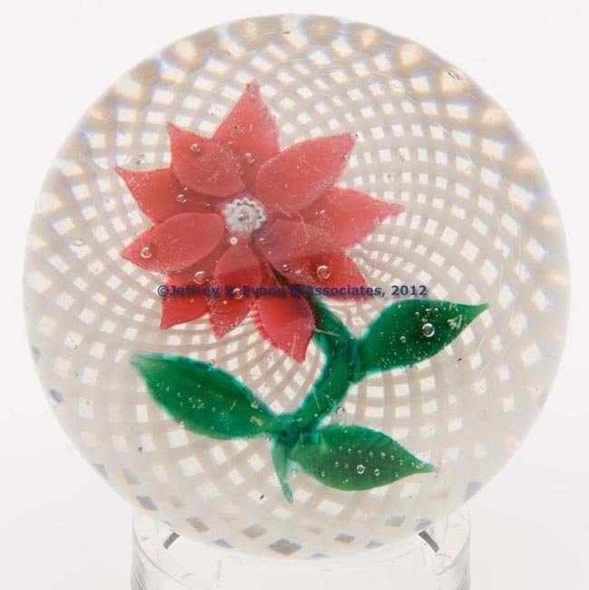 NEW ENGLAND POINSETTIA PAPERWEIGHT: NEW ENGLAND POINSETTIA PAPERWEIGHT, ten-petal flower with three green leaves and a stem, dew-like controlled bubbles, all on a white latticinio ground, concave base with a polished pontil mark. New En