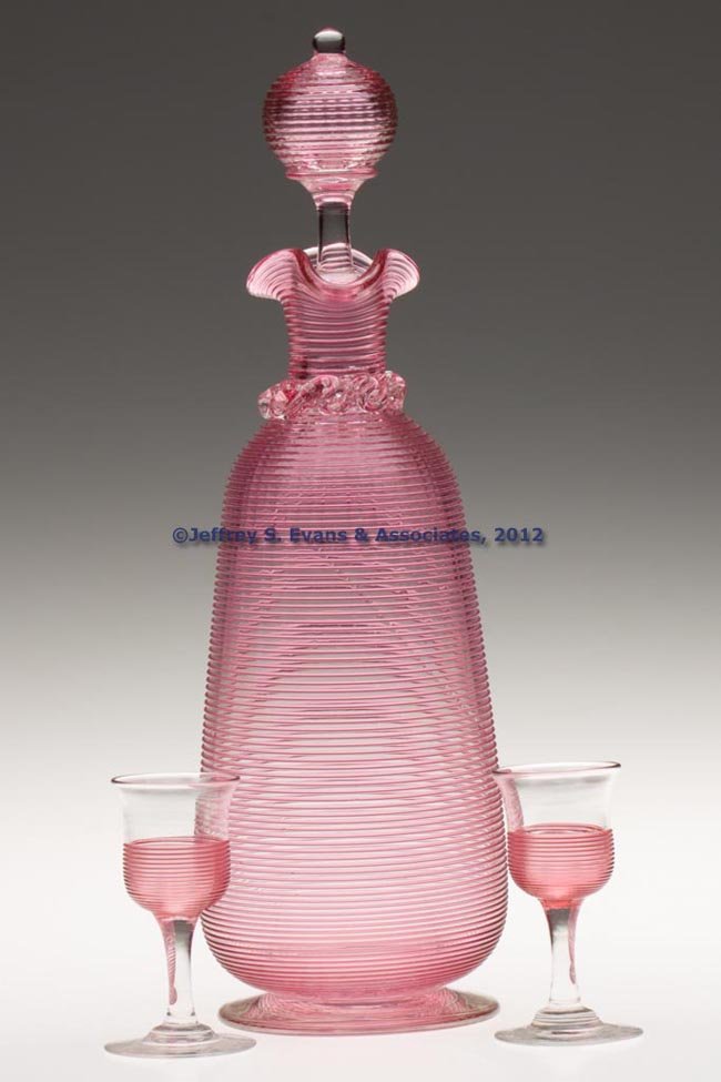 THREADED CORDIAL DECANTER AND TWO GLASSES: THREADED CORDIAL DECANTER AND TWO GLASSES, colorless with cranberry, decanter with applied rigaree collar, original stopper, and applied low foot with polished pontil mark, cordial glasses also with p