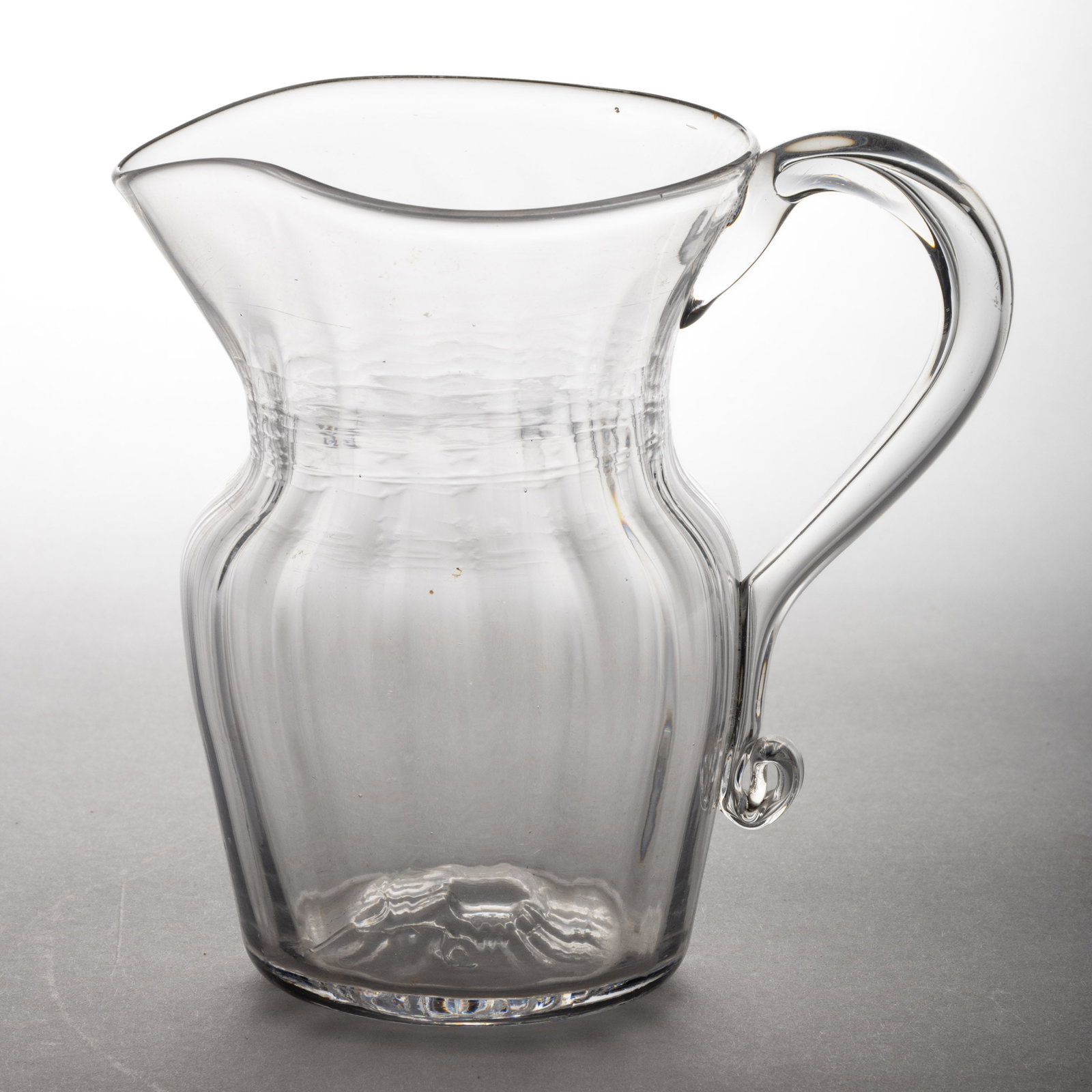 PATTERN-MOLDED PITCHER: PATTERN-MOLDED PITCHER, colorless, shouldered form with 16 vertical ribs, applied hollow handle with a curl to the lower terminal of the handle, rough pontil mark. Pittsburgh area. First hal