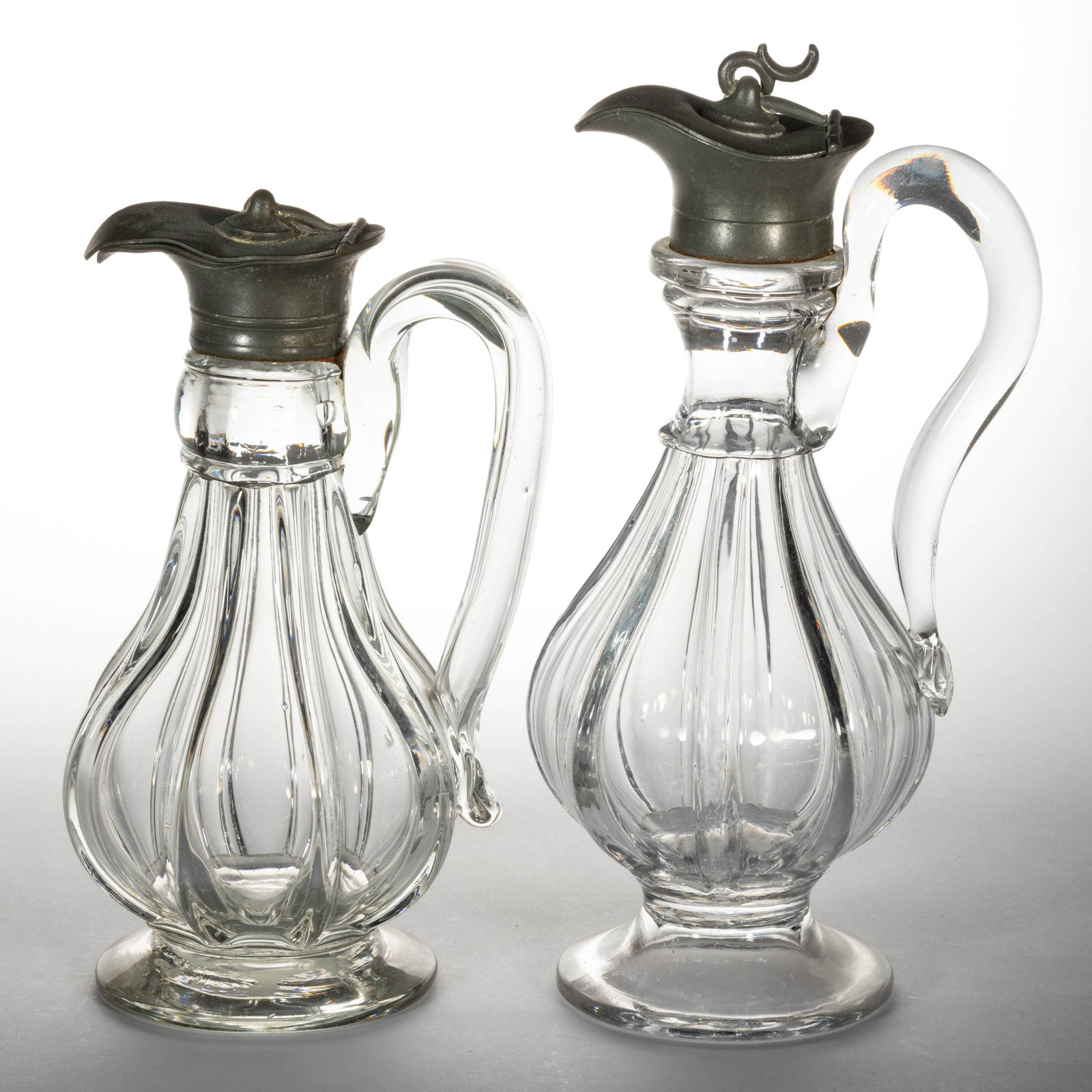 PATTERN-MOLDED GLASS SYRUP PITCHERS / CANS, LOT OF TWO: PATTERN-MOLDED GLASS SYRUP PITCHERS / CANS, LOT OF TWO, colorless, each being baluster-form with one having a waisted neck, each having vertical ribs, applied handles, and a period lid. Pittsburgh are