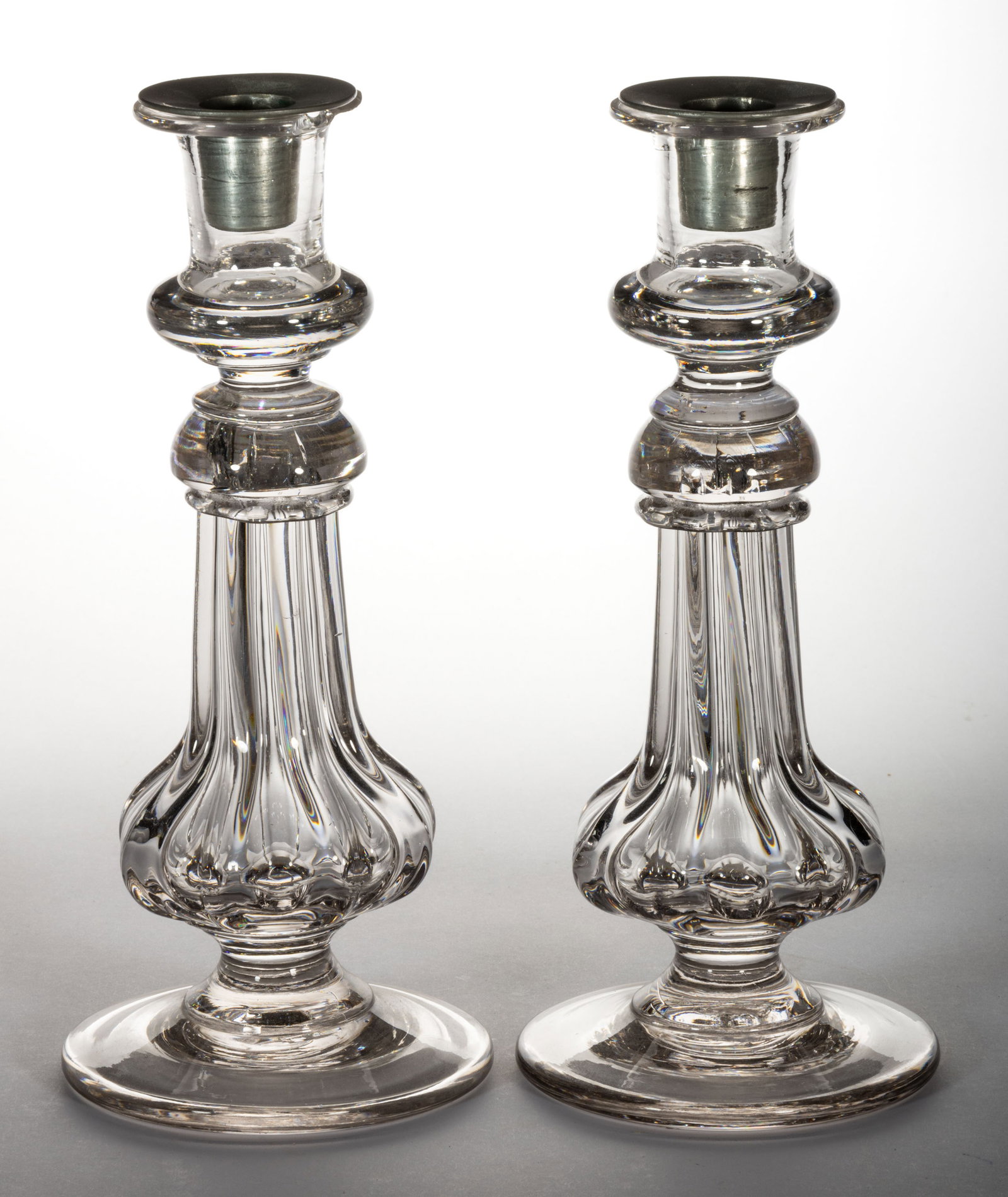 PILLAR-MOLDED PAIR OF CANDLESTICKS: PILLAR-MOLDED PAIR OF CANDLESTICKS, colorless, each having a solid-base socket with a waisted connector and tear-drop standard with a large circular foot, rough pontil mark, pewter socket inserts. Att