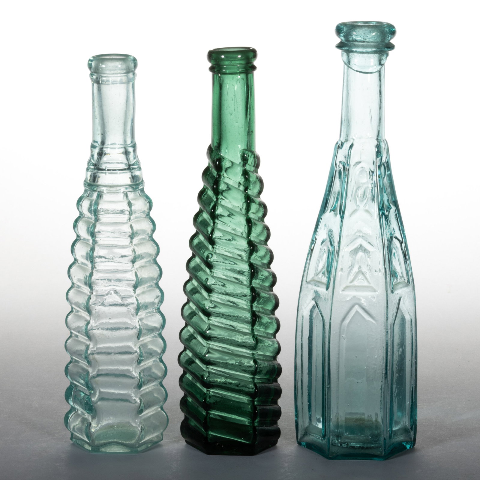 BLOWN-MOLDED PEPPER SAUCE BOTTLES, LOT OF THREE: BLOWN-MOLDED PEPPER SAUCE BOTTLES, LOT OF THREE, comprising an aquamarine Gothic Arch, an aquamarine ribbed, and an emerald green swirled rib example. Various makers. 19th century. 8 1/8" to 8 3/4" H.