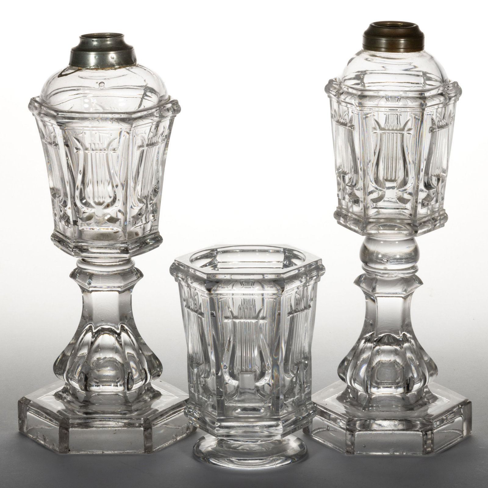 PRESSED LYRE / HARP WHALE OIL / FLUID STAND LAMPS, LOT OF TWO: PRESSED LYRE / HARP WHALE OIL / FLUID STAND LAMPS, LOT OF TWO, colorless lead glass, comprising a large and small size with each being raised on a hexagonal baluster-form stem and base, wafer construc
