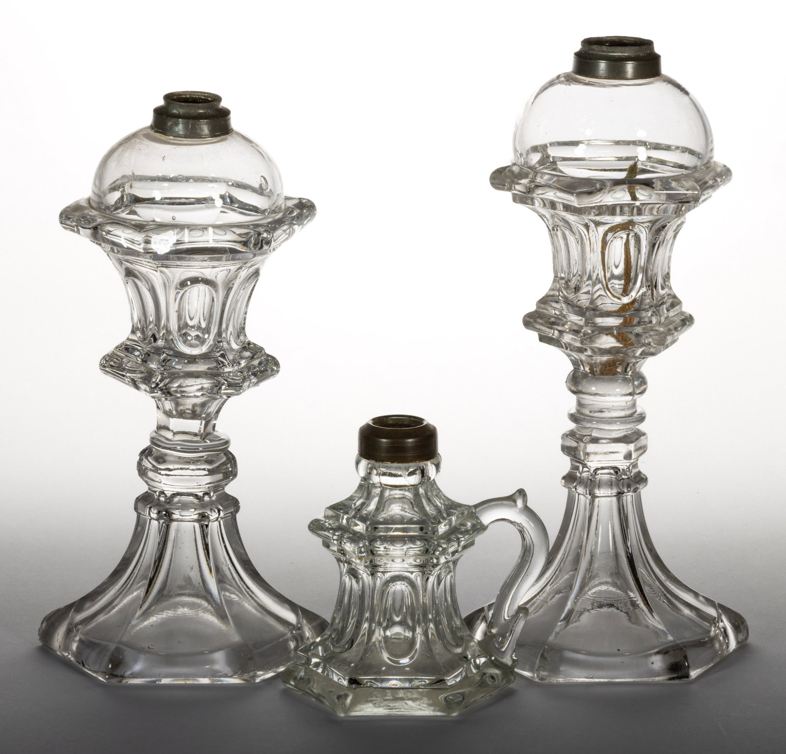 PRESSED WAISTED LOOP WHALE OIL / FLUID LAMPS, LOT OF THREE: PRESSED WAISTED LOOP WHALE OIL / FLUID LAMPS, LOT OF THREE, colorless lead glass, comprising two stand lamps with domed fonts and raised on flaring hexagonal bases, and a waisted finger lamp, each hav