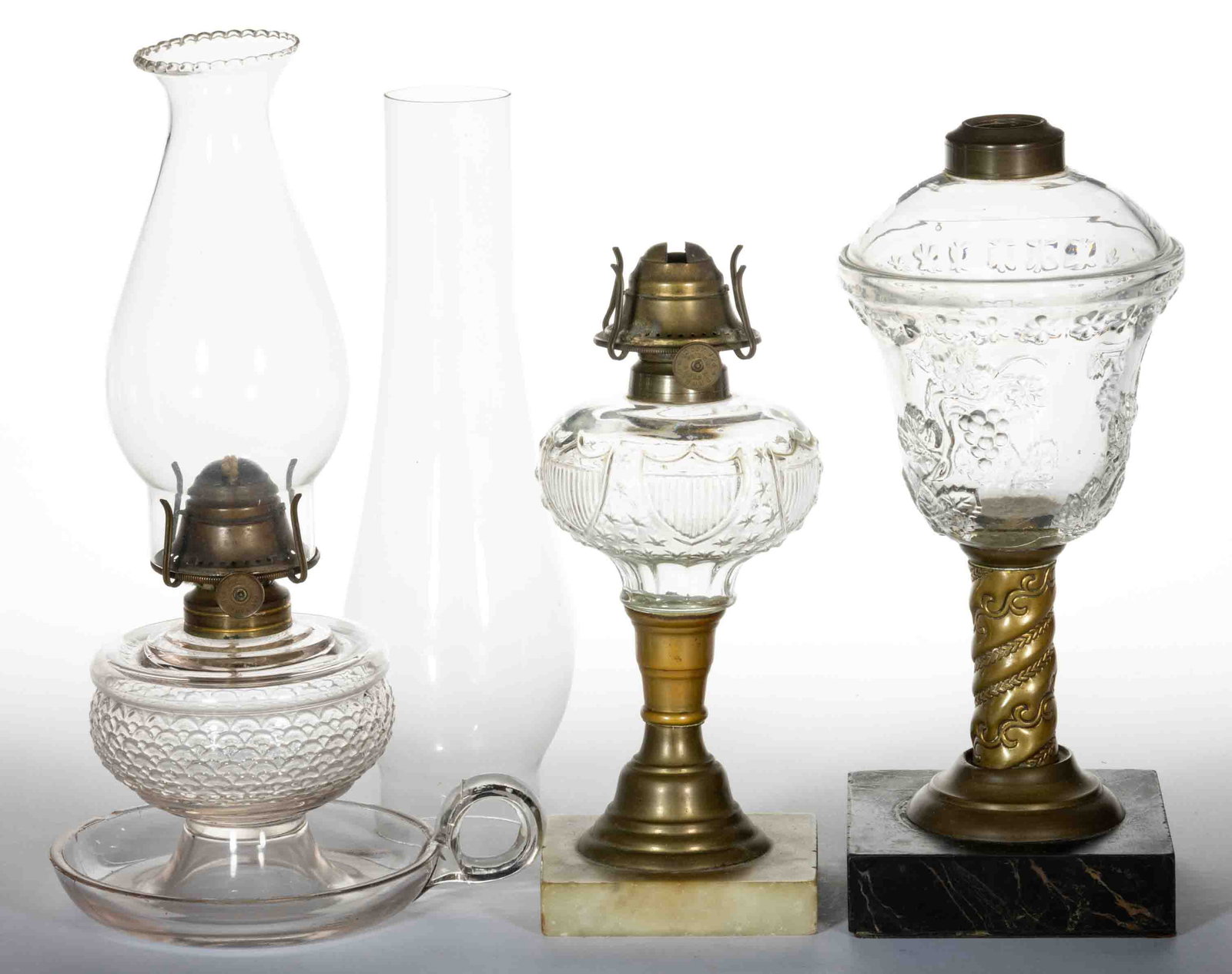 ASSORTED GLASS KEROSENE LAMPS, LOT OF THREE: ASSORTED GLASS KEROSENE LAMPS, LOT OF THREE, colorless, comprising a Shield and Stars stand lamp, a Fishscale finger lamp, and a Grapevine stand lamp, two fitted with a period slip burner and colorles