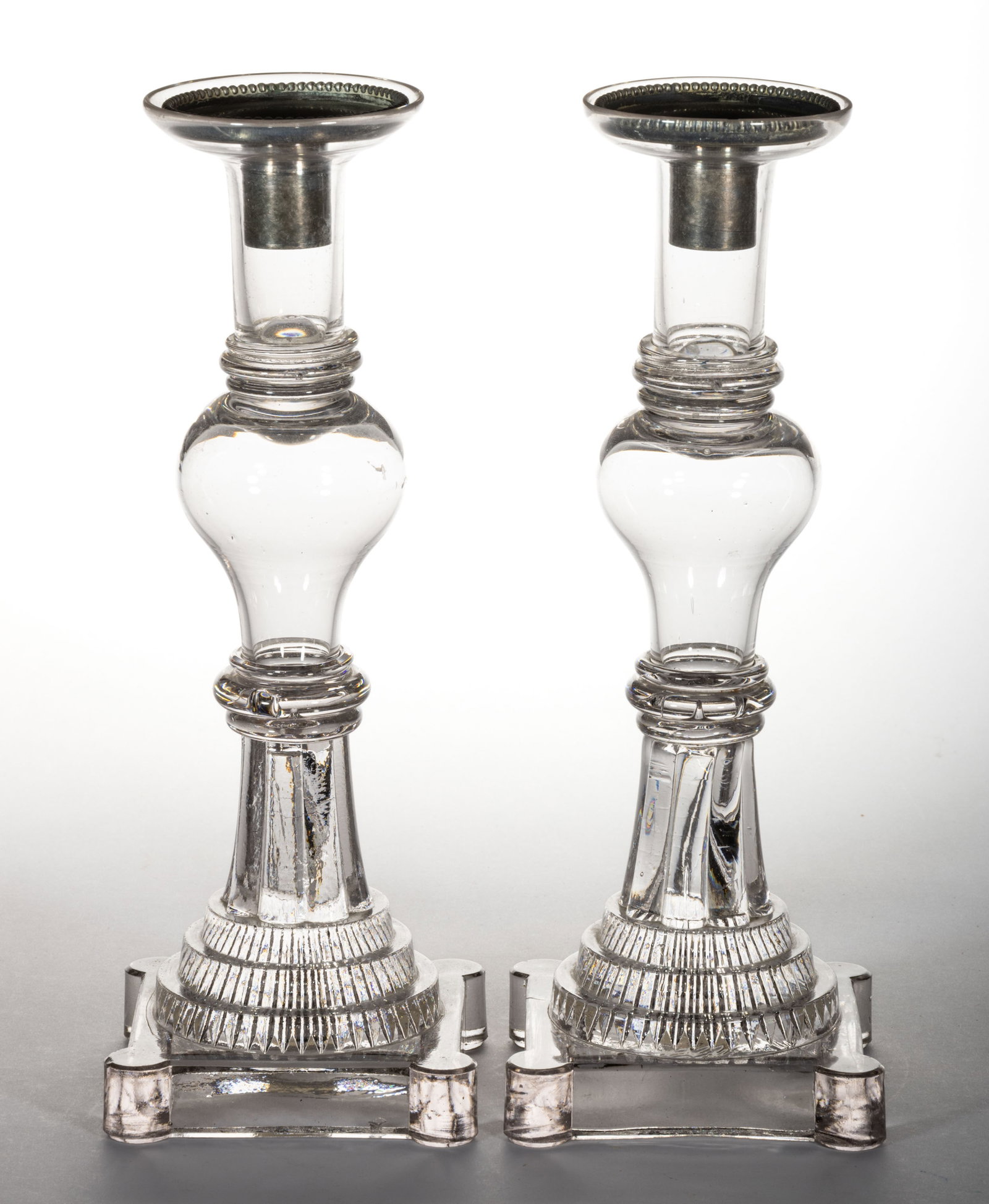 FREE-BLOWN AND PRESSED PAIR OF CANDLESTICKS: FREE-BLOWN AND PRESSED PAIR OF CANDLESTICKS, colorless, each deep, gallery-rim socket raised on a hollow, inverted pyriform knop, and stepped square base with rounded corners, ringed wafer constructio