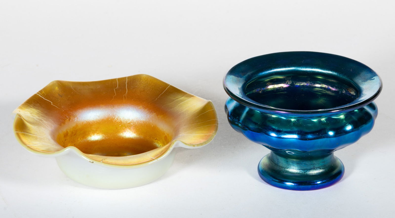 IRIDESCENT ART GLASS OPEN SALTS, LOT OF TWO: IRIDESCENT ART GLASS OPEN SALTS, LOT OF TWO, comprising a Steuben Gold Calcite, and a blue iridescent studio art glass footed example. 19th and 20th century. 1 1/8" to 1 3/4" H. Provena