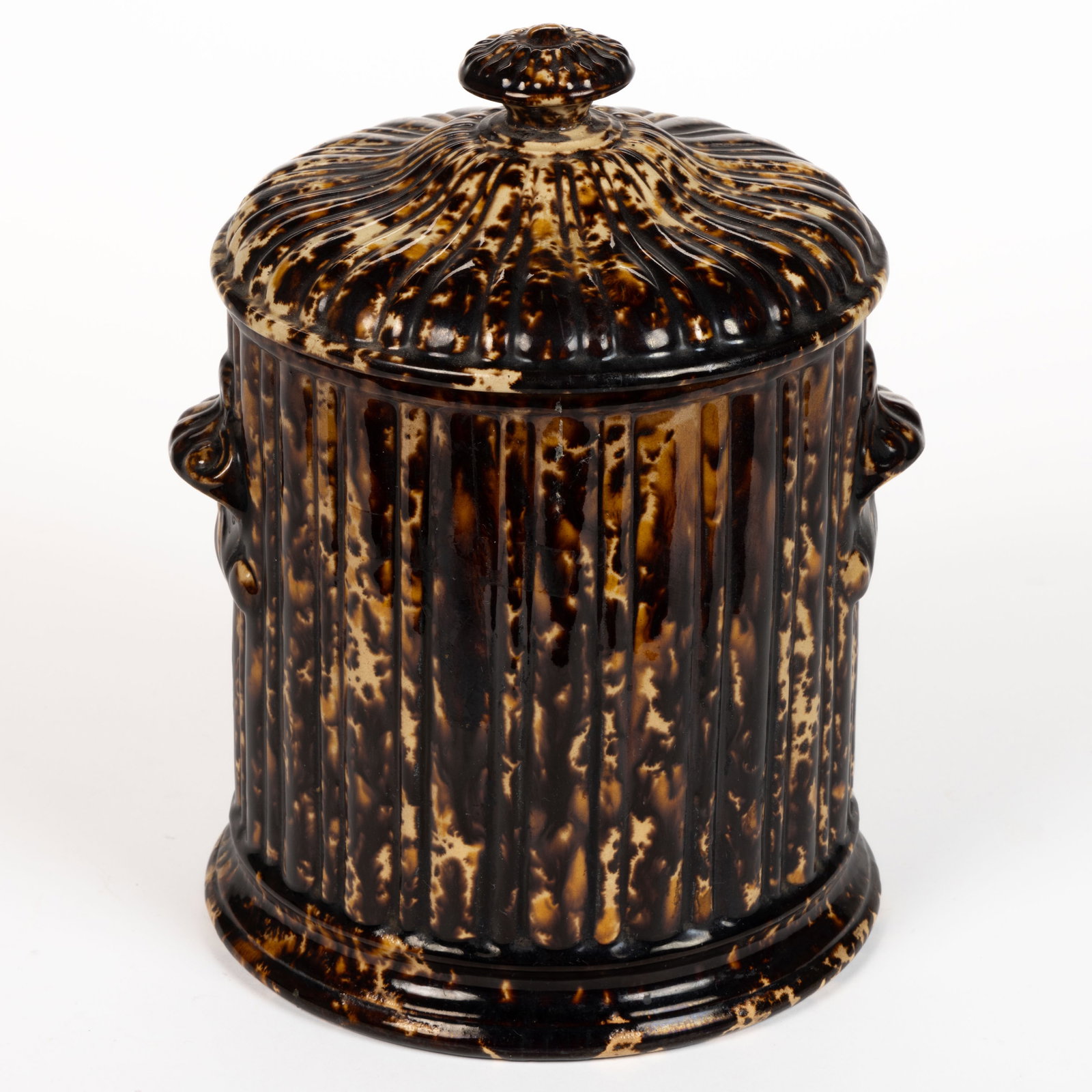 AMERICAN STAMPED BENNINGTON FLINT ENAMEL ROCKINGHAM-GLAZED POTTERY COVERED TOBACCO JAR: AMERICAN STAMPED BENNINGTON FLINT ENAMEL ROCKINGHAM-GLAZED POTTERY COVERED TOBACCO JAR, mottled brown and orange glazes, alternate rib pattern with molded horizontal scrolled handles. Having fain
