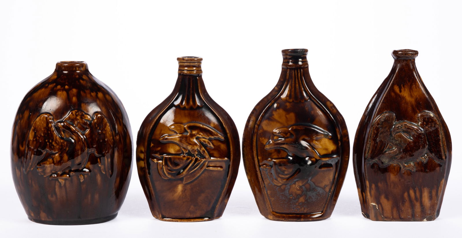 AMERICAN ROCKINGHAM-GLAZED POTTERY EAGLE MOTIF BOTTLES / FLASKS, LOT OF FOUR: AMERICAN ROCKINGHAM-GLAZED POTTERY EAGLE MOTIF BOTTLES / FLASKS, LOT OF FOUR, mottled brown glaze, comprising two featuring a bird perched to flags on one side and opposite having differing flora