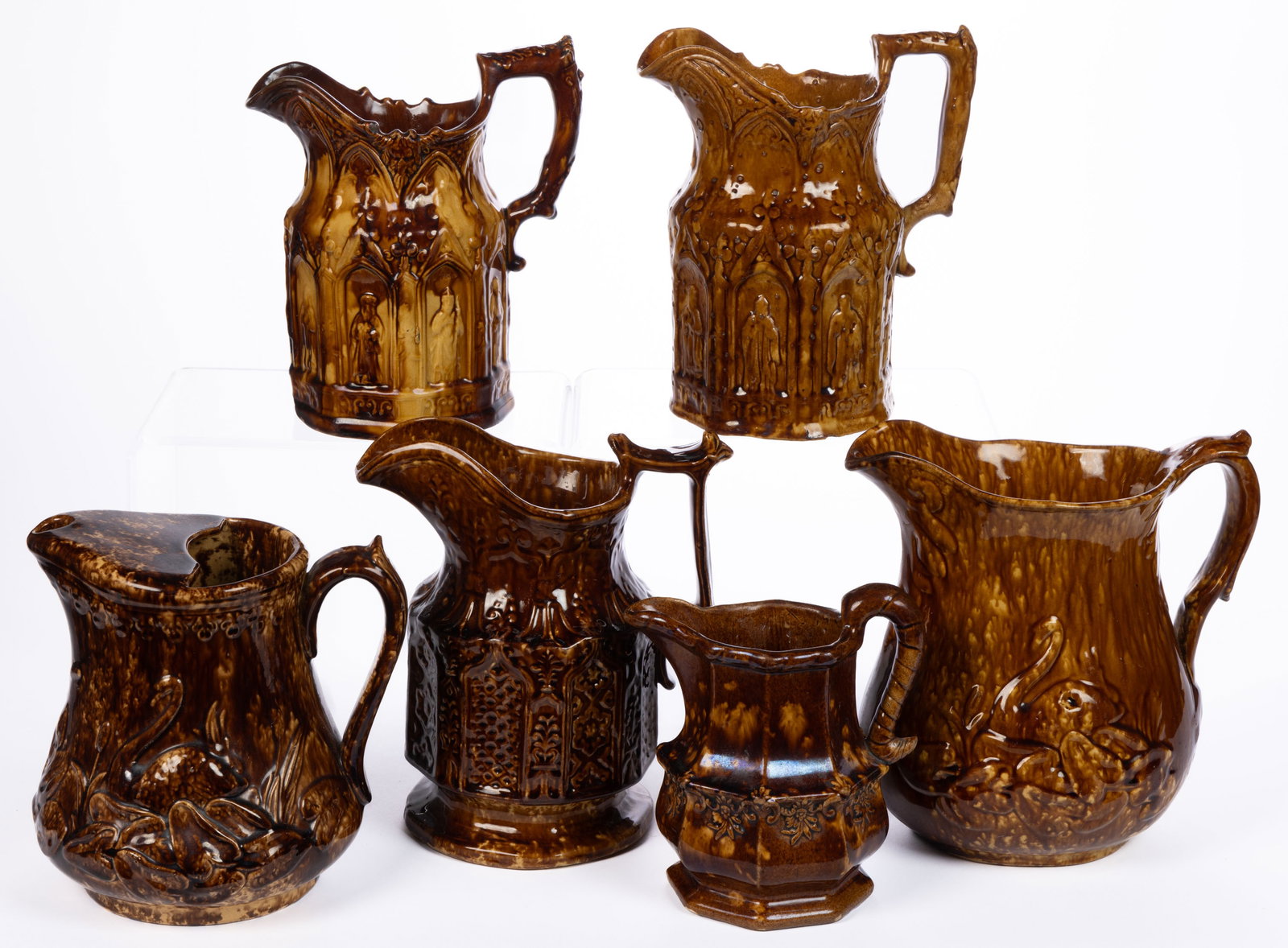 AMERICAN ROCKINGHAM-GLAZED POTTERY JUGS / PITCHERS, LOT OF SIX: AMERICAN ROCKINGHAM-GLAZED POTTERY JUGS / PITCHERS, LOT OF SIX, each mottled brown, including two panel-form examples featuring gothic architecture and the eight apostles, attributed to the Ameri
