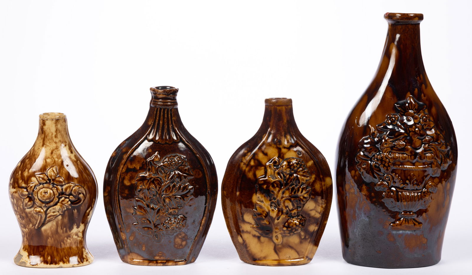AMERICAN ROCKINGHAM-GLAZED POTTERY FLORAL MOTIF BOTTLES / FLASKS, LOT OF FOUR: AMERICAN ROCKINGHAM-GLAZED POTTERY FLORAL MOTIF BOTTLES / FLASKS, LOT OF FOUR, mottled brown glaze, comprising two examples with flower and berry designs, a baluster-form example with rose image, and