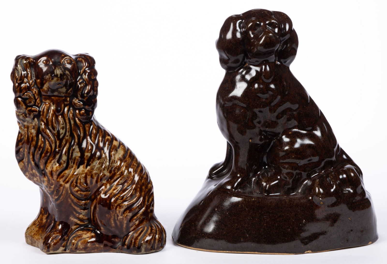 AMERICAN EARTHENWARE DOG / SPANIEL FIGURES, LOT OF TWO: AMERICAN EARTHENWARE DOG / SPANIEL FIGURES, LOT OF TWO, each sitting with tail around hind legs and wearing a collar with locket, comprising one dark brown-glazed example on an ovoid base, open-bottom