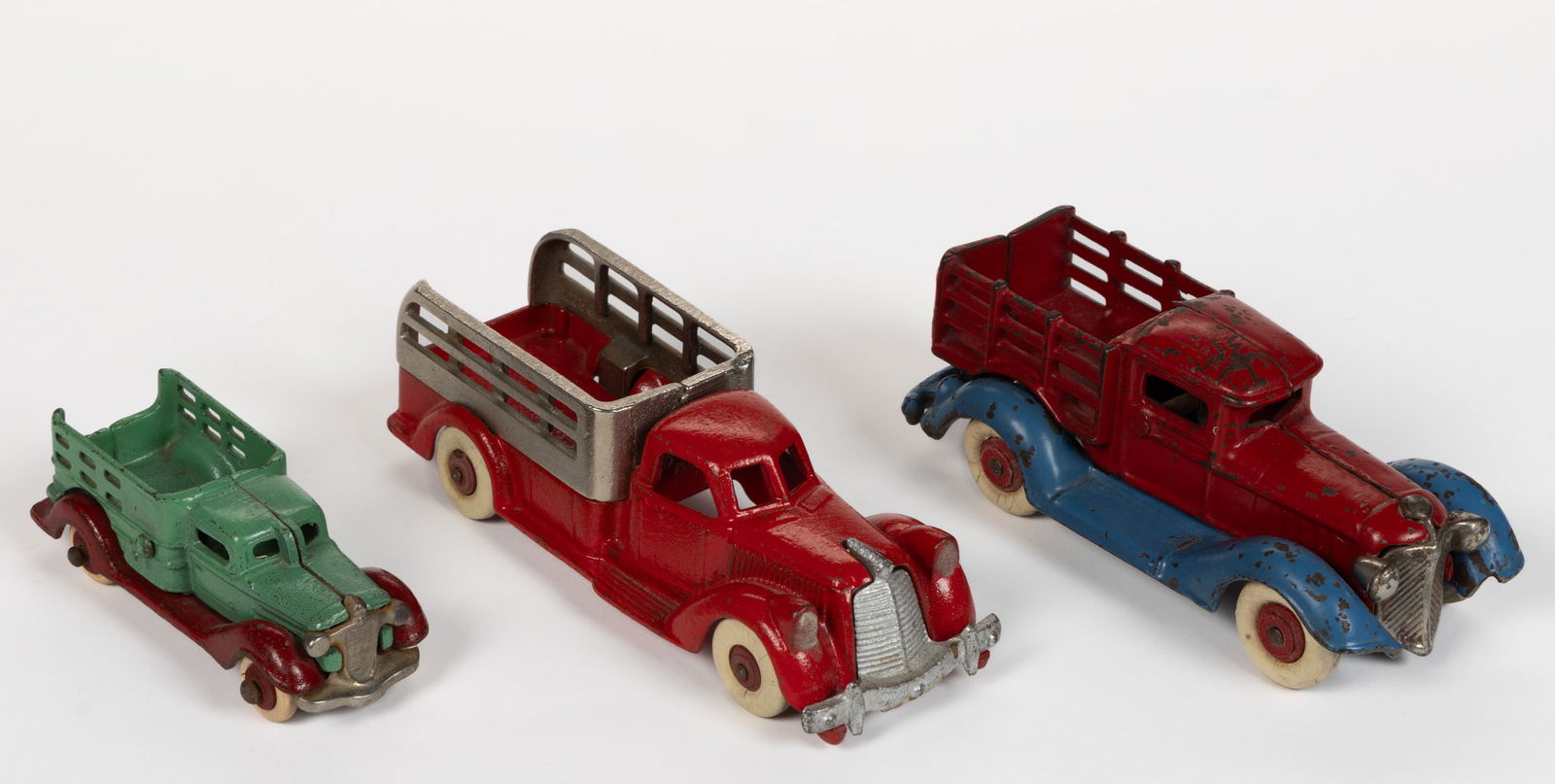 ASSORTED MANUFACTURERS CAST-IRON STAKE BED TOY TRUCKS, LOT OF THREE (1 of 2)