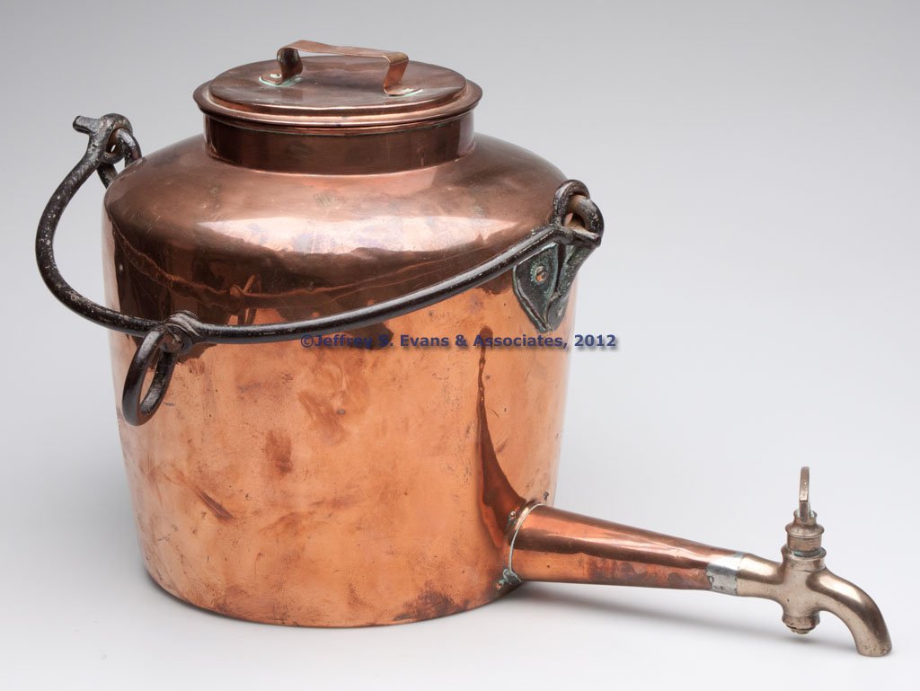 COPPER HANGING HOT-WATER KETTLE: COPPER HANGING HOT-WATER KETTLE, dovetailed body with applied and riveted spout, brass spigot marked Hickman, and wrought-iron bail handle, lid with a strap handle. First half 19th century. 12" H to r