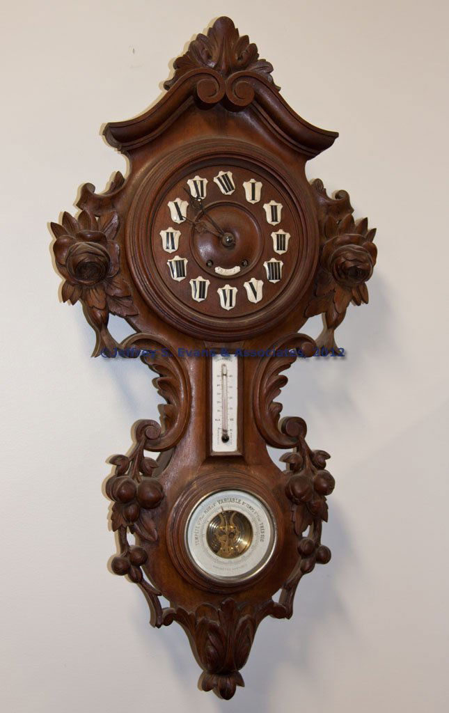 BLACK FOREST CARVED WALNUT WALL CLOCK: BLACK FOREST CARVED WALNUT WALL CLOCK, additional porcelain thermometer and lower barometer, wooden dial with applied porcelain numerals and name plate, original key and pendulum. Fourth quarter 19th