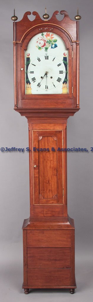 VIRGINIA OR TENNESSEE SHERATON CHERRY TALL-CASE CL: VIRGINIA OR TENNESSEE SHERATON CHERRY TALL-CASE CLOCK, brass and wood works with two winding holes, case constructed in three sections, the hood displaying an unusual double broken-arch pediment, four