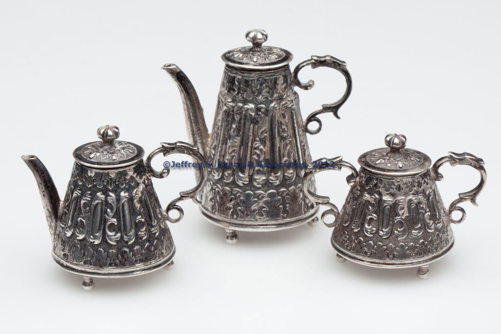 CONTINENTAL SILVER MINIATURE THREE-PIECE TEA SET: CONTINENTAL SILVER MINIATURE THREE-PIECE TEA SET, comprising two pots and a sugar bowl, each with repousse decoration and various hallmarks. Total weight: 2.13 ozt. 20th century. 1 3/8" to 2 1/8" H. P