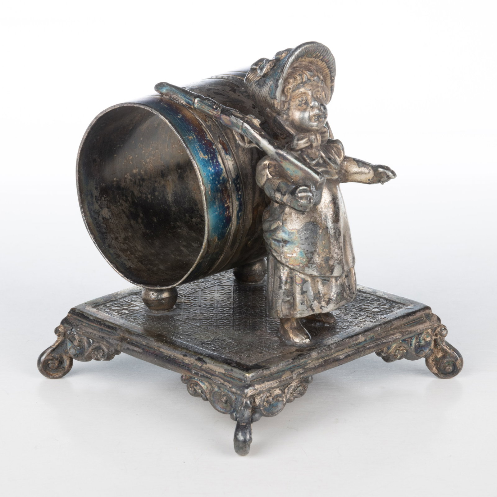 SIMPSON, HALL, MILLER & CO. KATE GREENAWAY-TYPE GIRL WITH RIFLE FIGURAL SILVER-PLATED NAPKIN RING: SIMPSON, HALL, MILLER & CO. KATE GREENAWAY-TYPE GIRL WITH RIFLE FIGURAL SILVER-PLATED NAPKIN RING, depicting a Kate Greenaway-type girl holding a toy rifle in her right arm in front of the napkin 