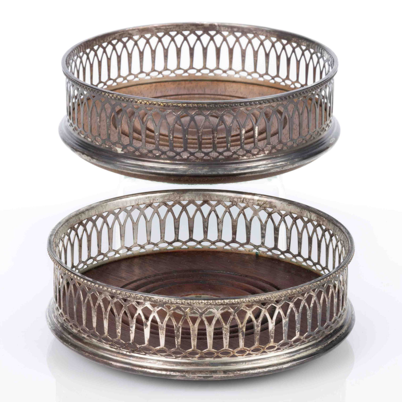 ENGLISH RETICULATED STERLING SILVER WINE BOTTLE COASTERS, NEAR PAIR: ENGLISH RETICULATED STERLING SILVER WINE BOTTLE COASTERS, NEAR PAIR, each round form, having a silver gallery rim with reticulated sides featuring arched designs, center with a turned walnut base, one