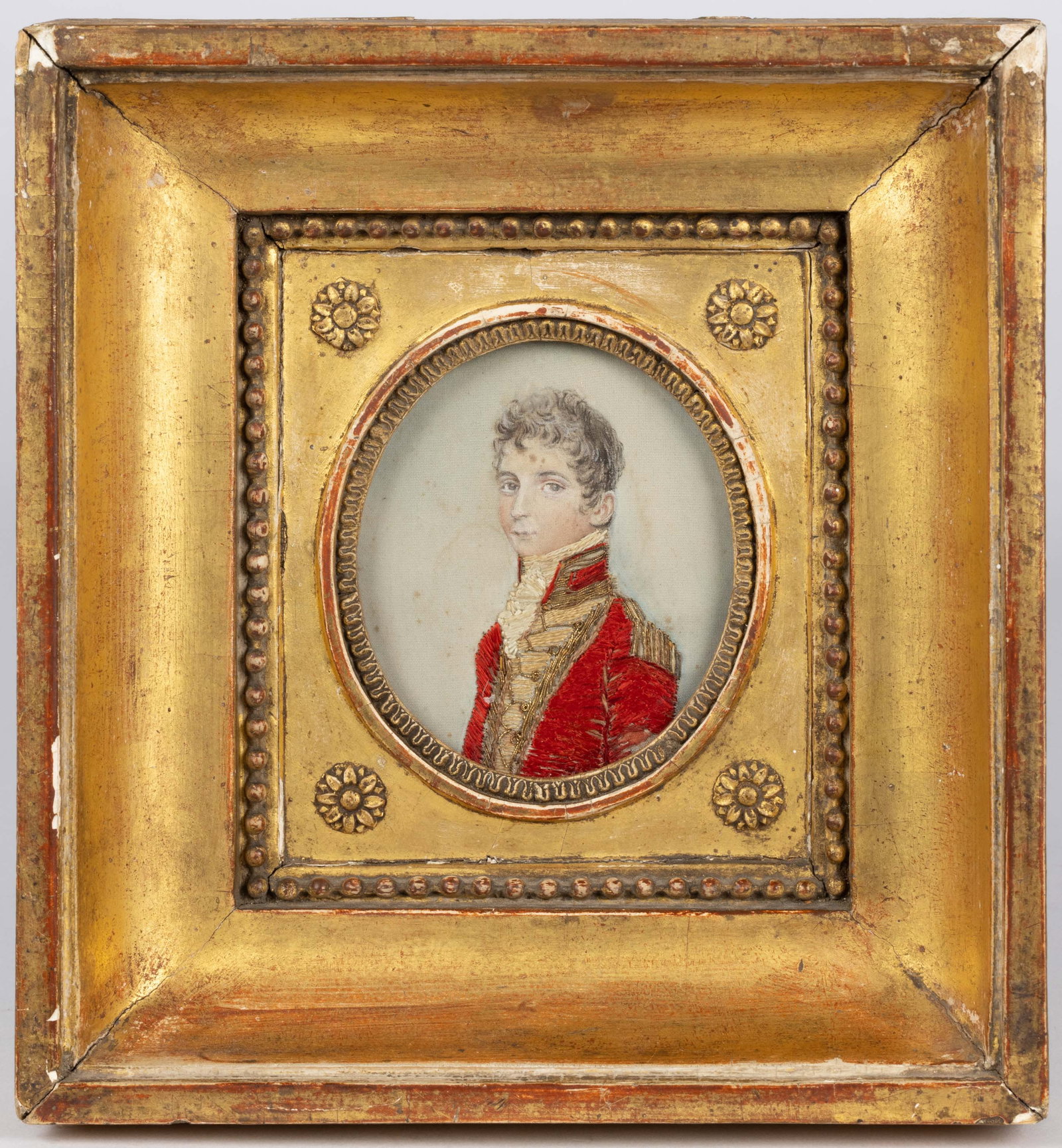 EUROPEAN SCHOOL (19TH CENTURY) MINIATURE PORTRAIT: EUROPEAN SCHOOL (19TH CENTURY) MINIATURE PORTRAIT, watercolor, silk and metallic-thread embroidery on silk, depicting a young military officer in a red coat. Housed under glass in a period giltwood fr