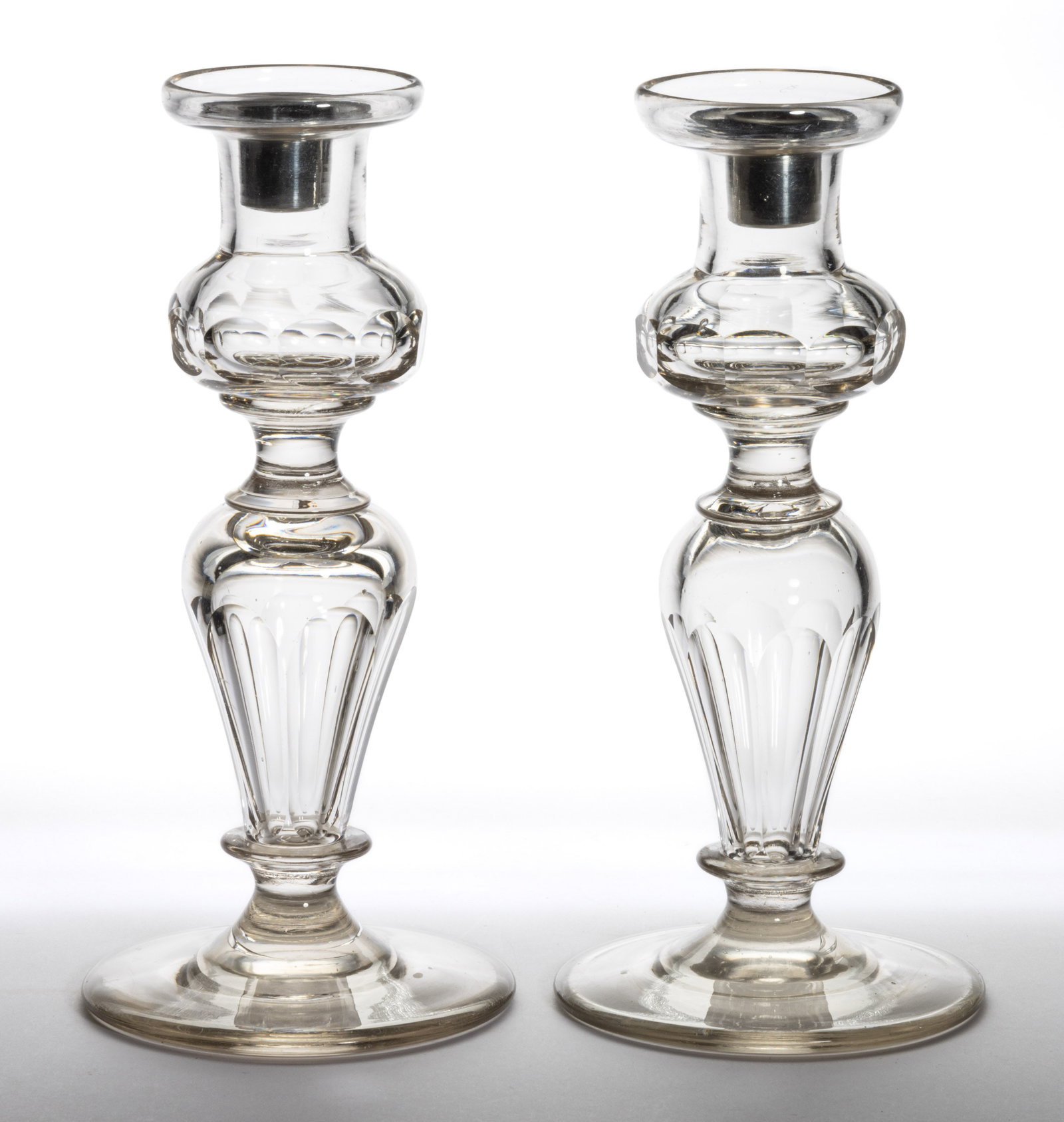 FREE-BLOWN AND CUT GLASS PAIR OF CANDLESTICKS: FREE-BLOWN AND CUT GLASS PAIR OF CANDLESTICKS, colorless, each having a deep thistle-form socket with a galleried rim and medial band of oval cuts, spool extension, with hollow inverted baluster stand