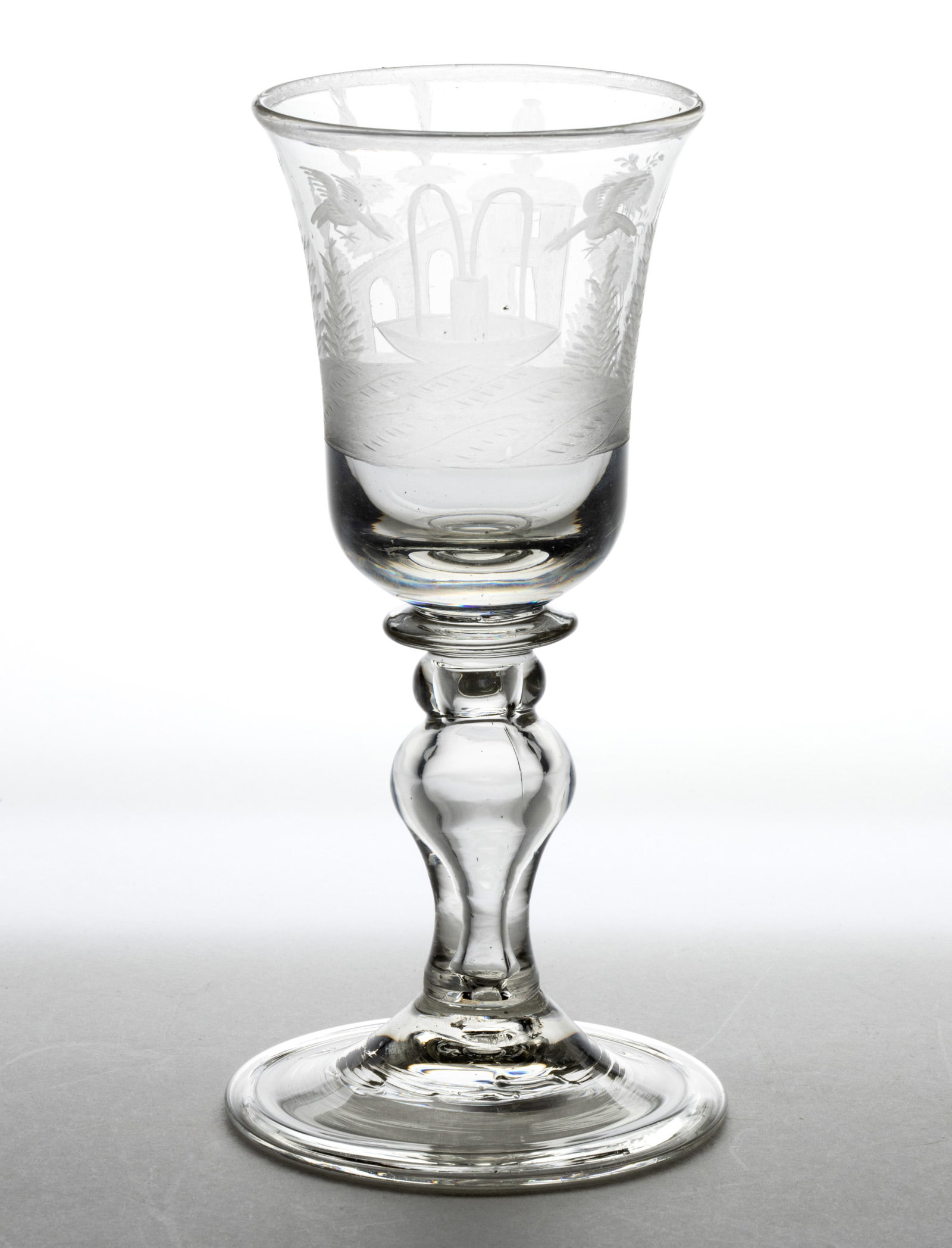 BOHEMIAN FREE-BLOWN AND ENGRAVED GLASS GOBLET: BOHEMIAN FREE-BLOWN AND ENGRAVED GLASS GOBLET, colorless soda-lime glass, bell-form bowl with engraved decoration featuring a fountain with two birds above and a building with two towers and a connect