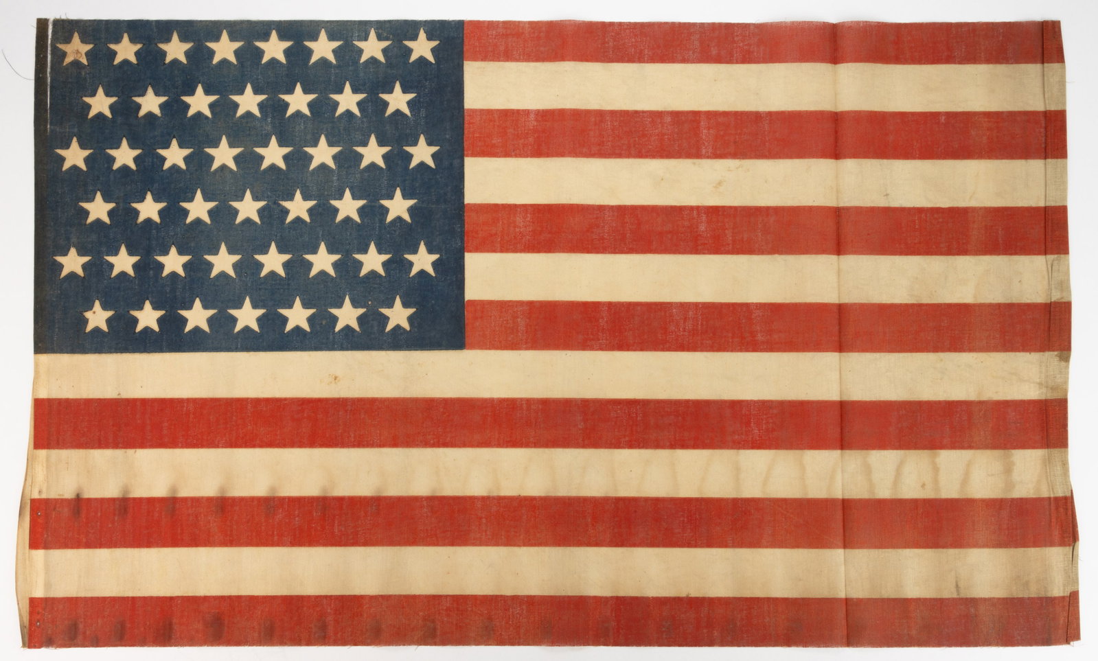 45-STAR AMERICAN NATIONAL UTAH STATEHOOD PRINTED PARADE FLAG: 45-STAR AMERICAN NATIONAL UTAH STATEHOOD PRINTED PARADE FLAG, glazed muslin, larger size, the canton exhibiting an 8/7/8/7/8/7 staggered linear pattern. Unframed. Circa 1896. 21" x 35". Prov
