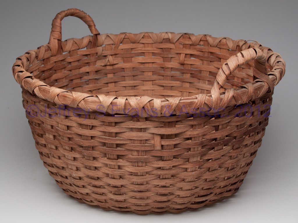 SHENANDOAH VALLEY OF VIRGINIA WOVEN SPLINT LAUNDRY: SHENANDOAH VALLEY OF VIRGINIA WOVEN SPLINT LAUNDRY BASKET, white oak, deep circular form with X-wrapped rim, two side handles and kick-up bottom. Original natural surface. Attributed to the Cook famil